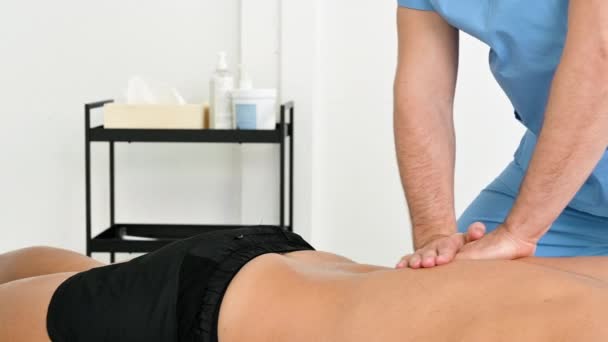 Fisioterapeuta massageando as costas de um jovem atleta na clínica de reabilitação esportiva. — Vídeo de Stock