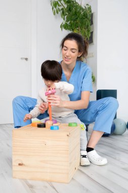 Rehabilitasyon hastanesinde fizyoterapist tarafından tedavi görürken engelli çocuk oyuncaklarla oynuyor..