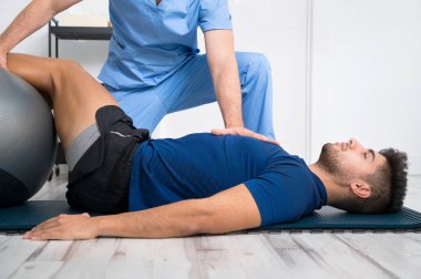 Fizyoterapist, genç ve yakışıklı hastaya pilates egzersizlerinde yardım ediyor..