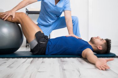Fizyoterapist, genç ve yakışıklı hastaya pilates egzersizlerinde yardım ediyor..