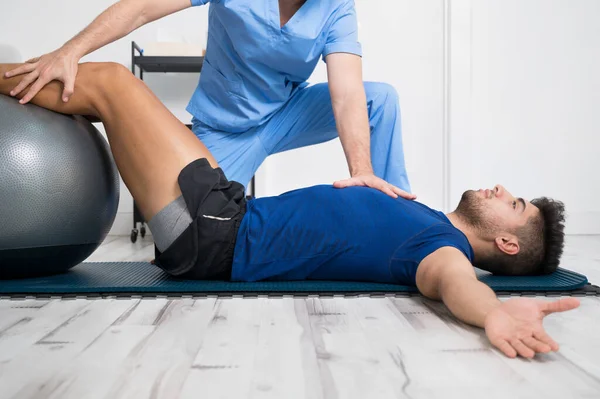 Fisioterapis membantu pasien muda tampan dengan latihan pilates. — Stok Foto