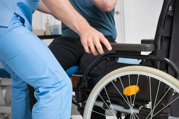 Male Physiotherapist helping a patient with a disability who uses a wheelchair to get up at rehabilitation hospital. — Stock Photo, Image