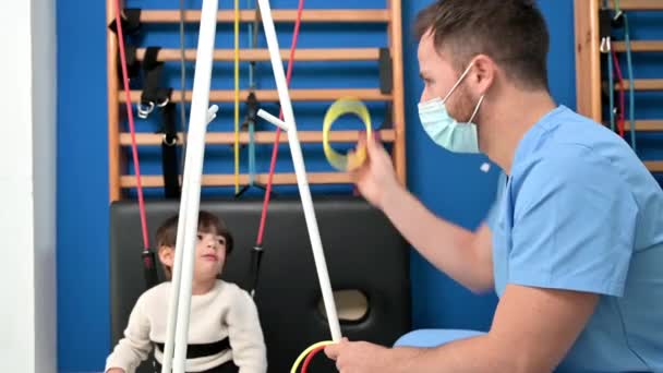 Ребенок с церебральным параличом по физиотерапии в детском терапевтическом центре. Мальчик с ограниченными возможностями, занимающийся упражнениями с помощью терапевта. — стоковое видео