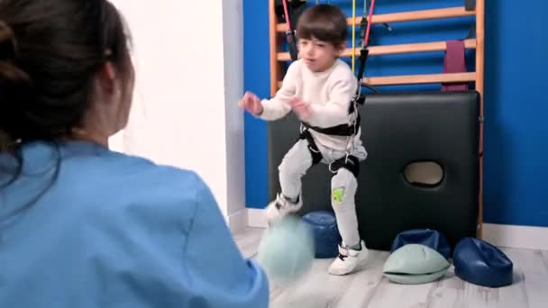 Az agyi bénulásban szenvedő kisgyereknek mozgásszervi terápiája van egy labdával végzett gyakorlatokkal, a test helyreállításával. Vidám fiú fogyatékossággal a rehabilitációs központban gyerekeknek — Stock videók