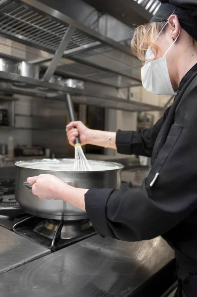 Health protection, safety and pandemic concept - Female chef cook wearing a protective face mask while working at restaurant kitchen. — Stock Photo, Image