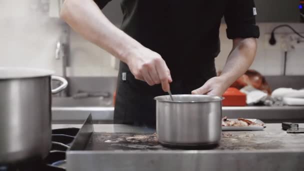 Dolly skudt, tæt på en uigenkendelig kok, der laver mad på panden i et kommercielt køkken. Filmisk nærbillede af varme kogepander med damp. – Stock-video