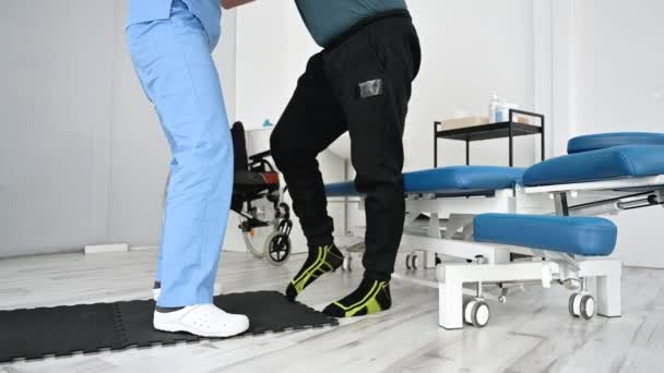 Hastanede rehabilitasyon sırasında yürürken orta yaşlı bir adamı tutan ve yardım eden fizyoterapist.. — Stok video