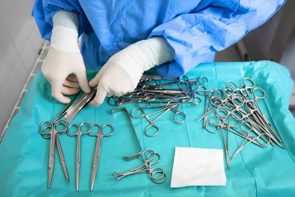 Mehrere chirurgische Instrumente auf blauem Tisch über der Ansicht. Chirurg nimmt chirurgisches Werkzeug vom Tisch. — Stockfoto