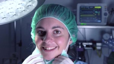 Hastanede ameliyat yapmadan önce maske takan ve kameraya bakıp gülümseyen yetişkin bir kadın..