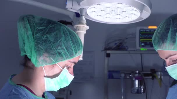 Chirurdzy żeńscy w mundurach medycznych przy użyciu profesjonalnych narzędzi stojących w jasnym świetle na sali operacyjnej — Wideo stockowe