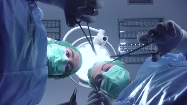 Από τα κάτω γυναίκες χειρουργοί σε ιατρική στολή χρησιμοποιώντας επαγγελματικά εργαλεία, ενώ στέκεται κάτω από έντονο φως στο χειρουργείο — Αρχείο Βίντεο