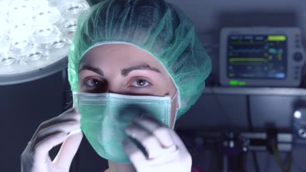 Dospělá žena v lékařské masce a klobouku hledá a usmívá se na kameru před provedením operace v nemocnici. — Stock video