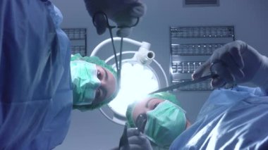 Ameliyathanede parlak ışık altında dururken profesyonel aletler kullanan doktor üniformalı kadın cerrahlardan.
