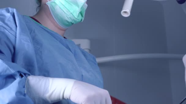 Tilt up shot de cirujanas en uniforme médico usando herramientas profesionales mientras están de pie bajo luz brillante en el quirófano — Vídeos de Stock