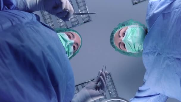 Από τα κάτω γυναίκες χειρουργοί σε ιατρική στολή χρησιμοποιώντας επαγγελματικά εργαλεία, ενώ στέκεται κάτω από έντονο φως στο χειρουργείο — Αρχείο Βίντεο
