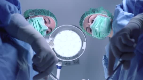Снизу женщины-хирурги в медицинской форме с помощью профессиональных инструментов, стоя под ярким светом в операционной — стоковое видео