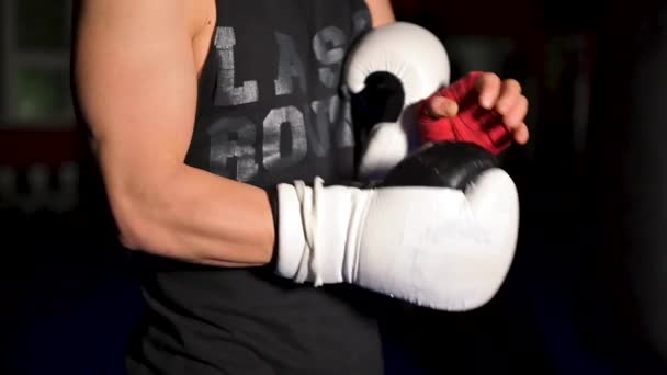 Muskulöser Mann in schwarzer Kleidung zieht sich vor einem Wettkampf lederne weiße Boxhandschuhe an die Hände. — Stockvideo