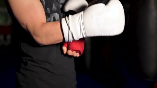 Muskulöser Mann in schwarzer Kleidung zieht sich vor einem Wettkampf lederne weiße Boxhandschuhe an die Hände. — Stockvideo