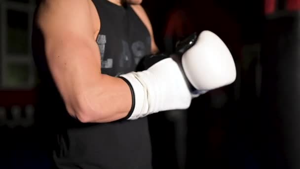Hombre musculoso en ropa negra se pone guantes de boxeo blancos de cuero en sus manos antes de una competición. — Vídeos de Stock