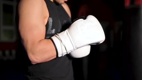 Hombre musculoso en ropa negra se pone guantes de boxeo blancos de cuero en sus manos antes de una competición. — Vídeo de stock