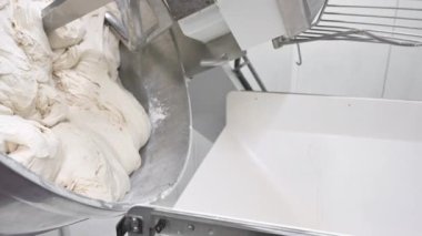 Büyük otomatik yoğurma makinesinden hamur dökülüyor. Ekmek ve un ürünleri üretimi kavramı, büyük miktarda.