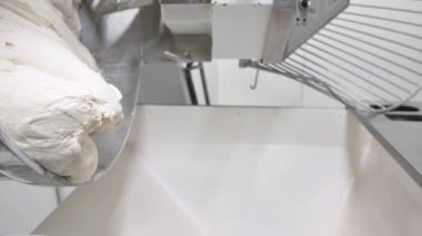 Büyük otomatik yoğurma makinesinden hamur dökülüyor. Ekmek ve un ürünleri üretimi kavramı, büyük miktarda.