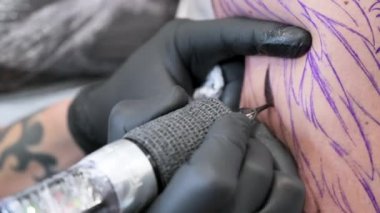 Salon dövmesi. Çalışan bir dövme sanatçısına yakın çekim. Dövmeci stüdyoda dövme yapıyor..