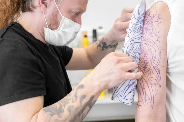 Tatuaje experto artista poner un boceto en el brazo de un hombre. — Foto de Stock