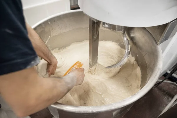 Пекарь вынимает тесто из смесительной машины в промышленной пекарне — стоковое фото