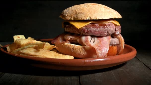 Hamburger di manzo grigliato premium con pancetta, formaggio e patatine fritte. Delizioso hamburger americano su sfondo di legno. Dolly ha sparato.. — Video Stock