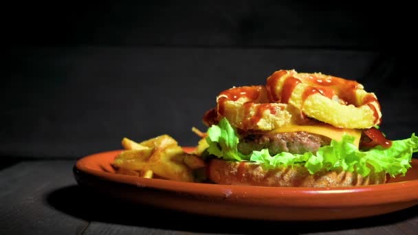 Primo piano di uno chef irriconoscibile che termina un hamburger di qualità Premium con anelli di cipolla, formaggio e salsa barbecue, servito con patatine fritte su un piatto rustico — Video Stock