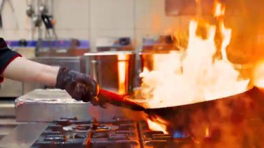 Şef elinde tava, tava, karıştırıyor, ateşle veya ateşle pişiriyor.