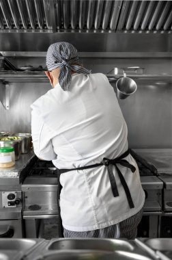 Bir restoranın mutfağında yemek pişiren kadın şefin arka manzarası..