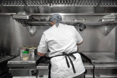 Bir restoranın mutfağında yemek pişiren kadın şefin arka manzarası..