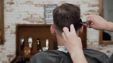 Berber genç ve yakışıklı bir adama makasla saç kesiyor. .