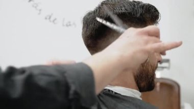 Berber genç ve yakışıklı bir adama makasla saç kesiyor. .