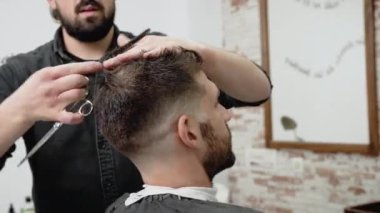 Berber genç ve yakışıklı bir adama makasla saç kesiyor. .