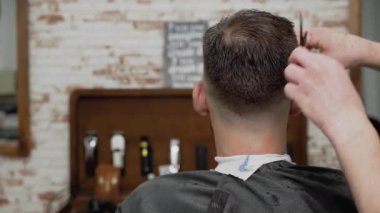 Berber genç ve yakışıklı bir adama makasla saç kesiyor. .