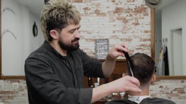 Berber genç ve yakışıklı bir adama makasla saç kesiyor. .