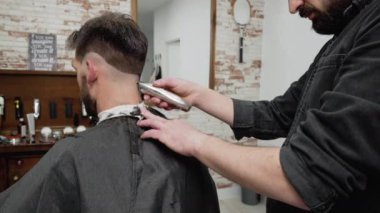 Erkek berber, berber dükkanında kırpıcıyla erkek müşterinin saçını kesiyor. Saç şekillendirme süreci. 