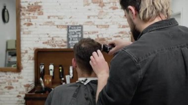 Erkek berber, berber dükkanında kırpıcıyla erkek müşterinin saçını kesiyor. Saç şekillendirme süreci. 