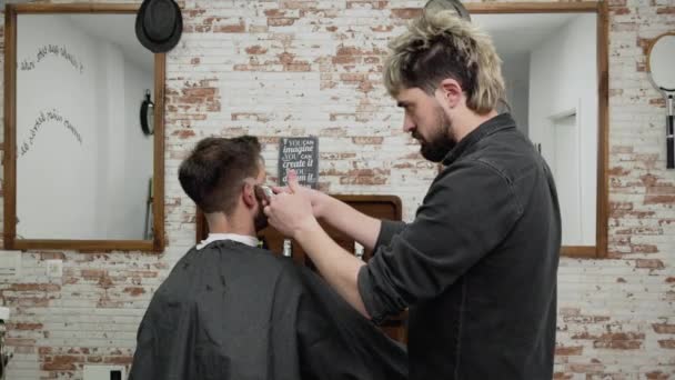 Seorang tukang cukur memotong rambut klien pria dengan gunting rambut di salon. Proses penataan rambut. — Stok Video
