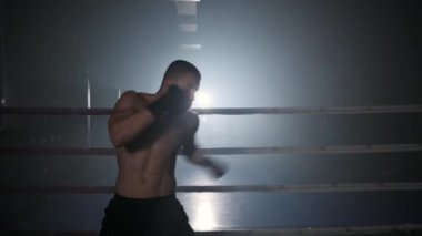 Profesyonel erkek kickboksör tek başına modern bir spor salonunda boks ringinde antrenman yapıyor..