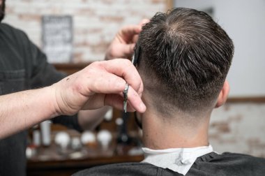 Berber genç ve yakışıklı bir adama makasla saç kesiyor. .