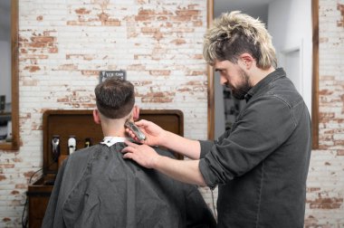 Erkek berber, berber dükkanında kırpıcıyla erkek müşterinin saçını kesiyor. Saç şekillendirme süreci. 