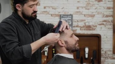 Berber genç ve yakışıklı bir adama makasla saç kesiyor. .