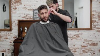 Erkek berber, berber dükkanında kırpıcıyla erkek müşterinin saçını kesiyor. Saç şekillendirme süreci. 