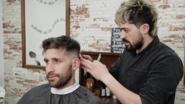 Erkek berber, berber dükkanında kırpıcıyla erkek müşterinin saçını kesiyor. Saç şekillendirme süreci. 