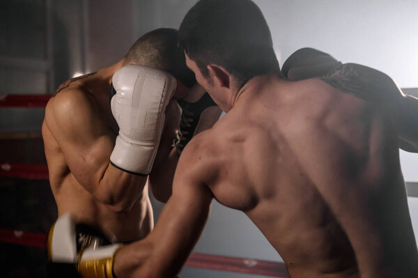 Two professional young muscular shirtless male boxers fighting in a boxing ring.