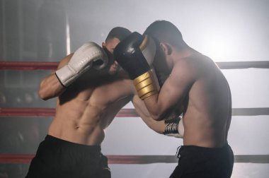 İki profesyonel genç kaslı üstsüz erkek boksör bir boks ringinde dövüşüyor..